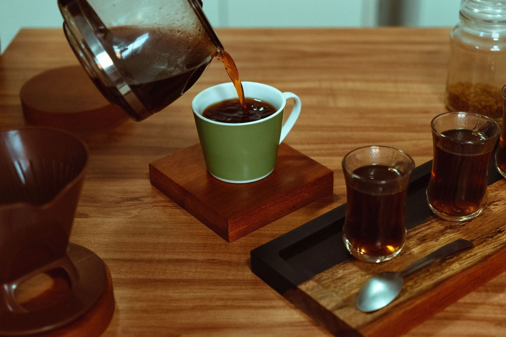 Kaffe hälls i en grön kopp bredvid flera glas med kaffe