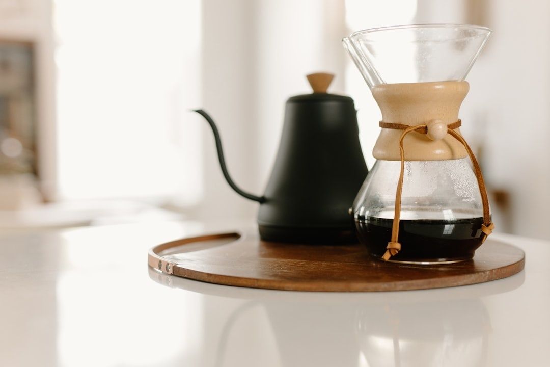 Glaskanna med bryggkaffe och svart hällpipkanna på träbricka